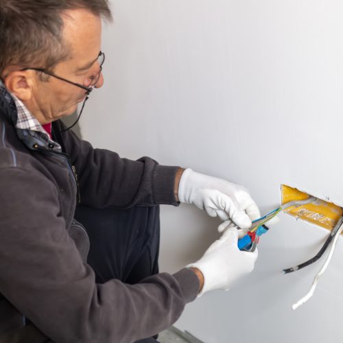 An electrician removes insulation from a copper wire. Working with the tool. Professional electrician working on electrical system, preparing copper wires for connection.